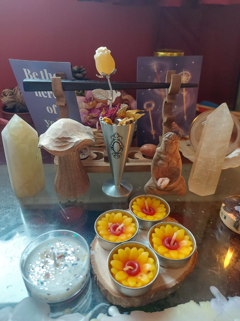 witch's altar featuring sunflower candles, citrine crystal points, magickal spell workings, a magic wand and wooden ornaments.